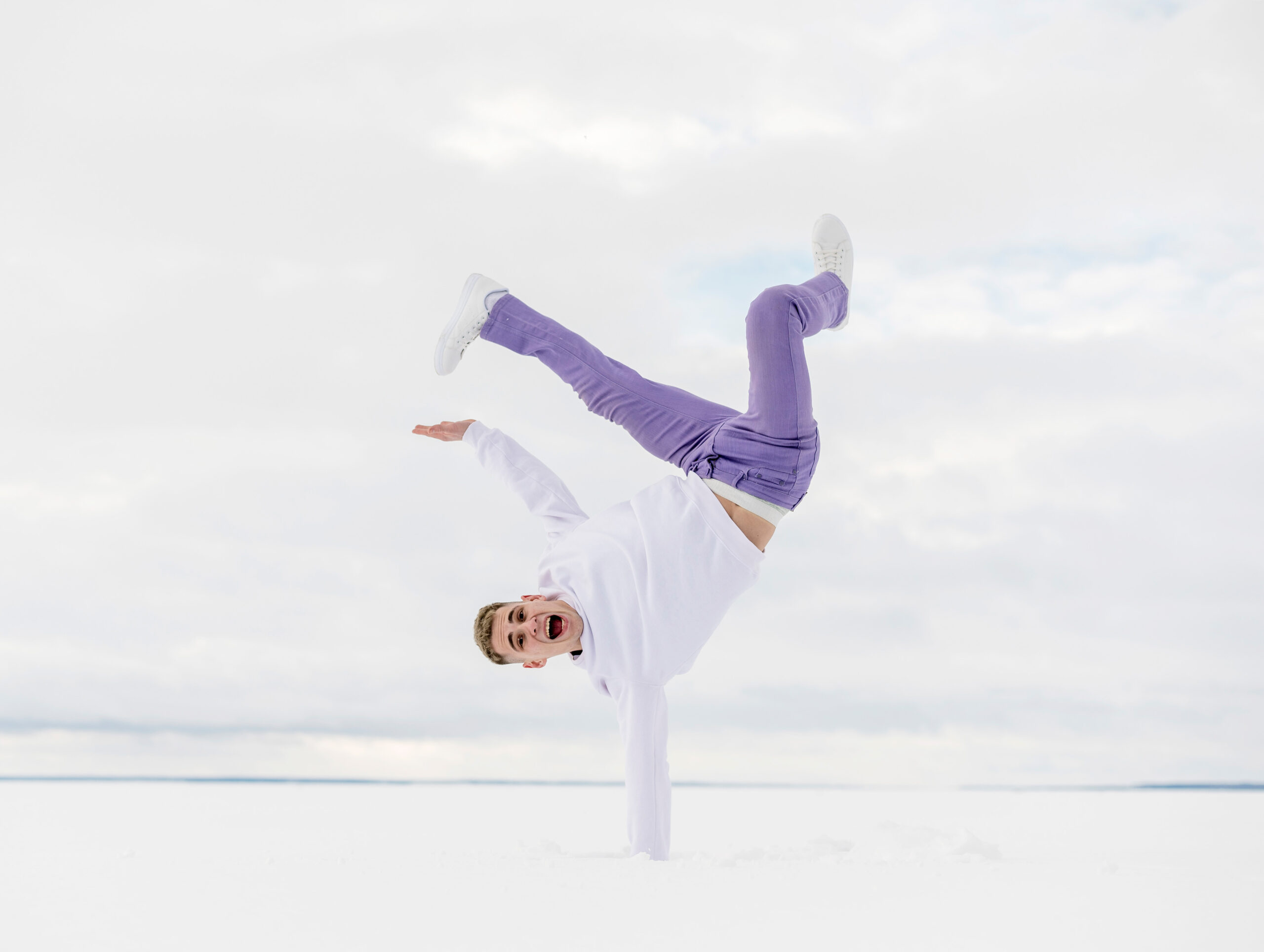 Ein junger Mann vollführt einen einhändigen Handstand im Schnee und schreit vor Freude – Ausdruck von Emotionen durch Tanz.