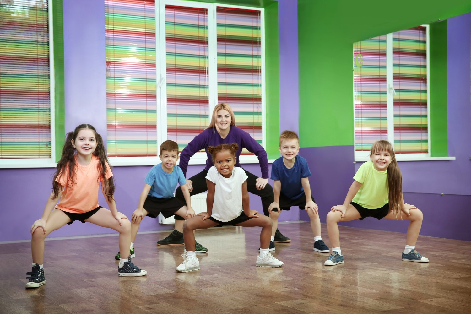 Eine Gruppe von Schulkindern tanzt gemeinsam mit einer Lehrerin in einem bunten Tanzstudio und trainiert rhythmische Koordination im groove2grow Unterricht.