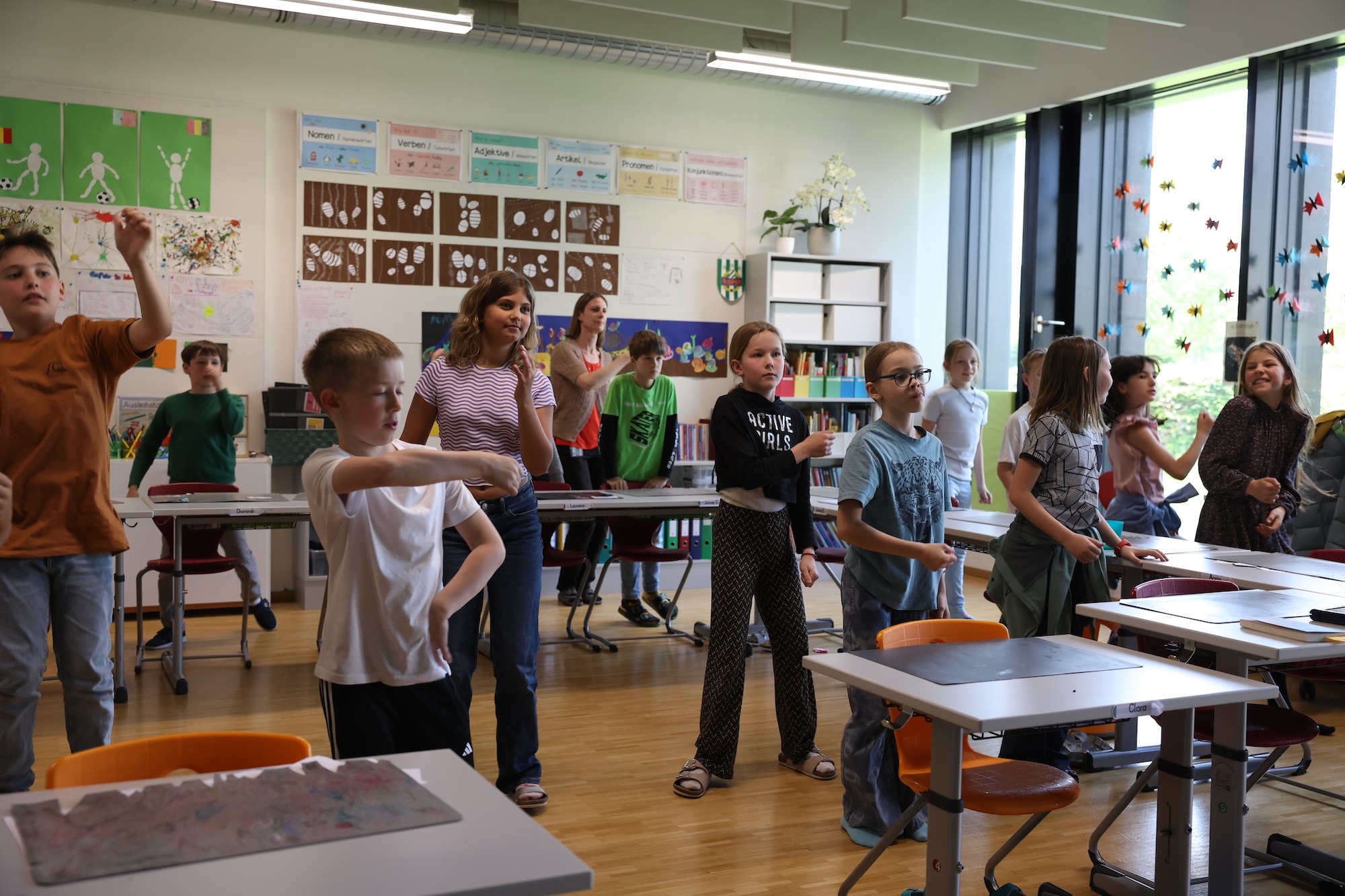 Eine Schülerin führt konzentriert eine Tanzbewegung in der Klasse aus, während andere Kinder im Hintergrund beobachten – ein Moment individueller Ausdruckskraft.