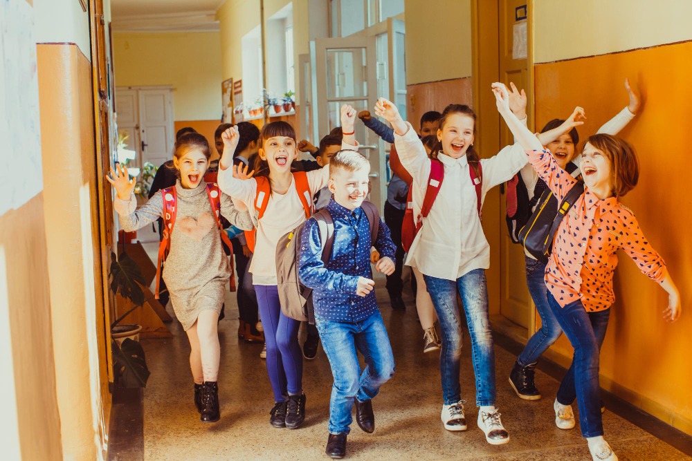 Flashmob-Projekt: Tanz bricht den Alltag Kinder laufen jubelnd und tanzend mit Rucksäcken durch einen sonnigen Schulflur – Aktion Flashmob.