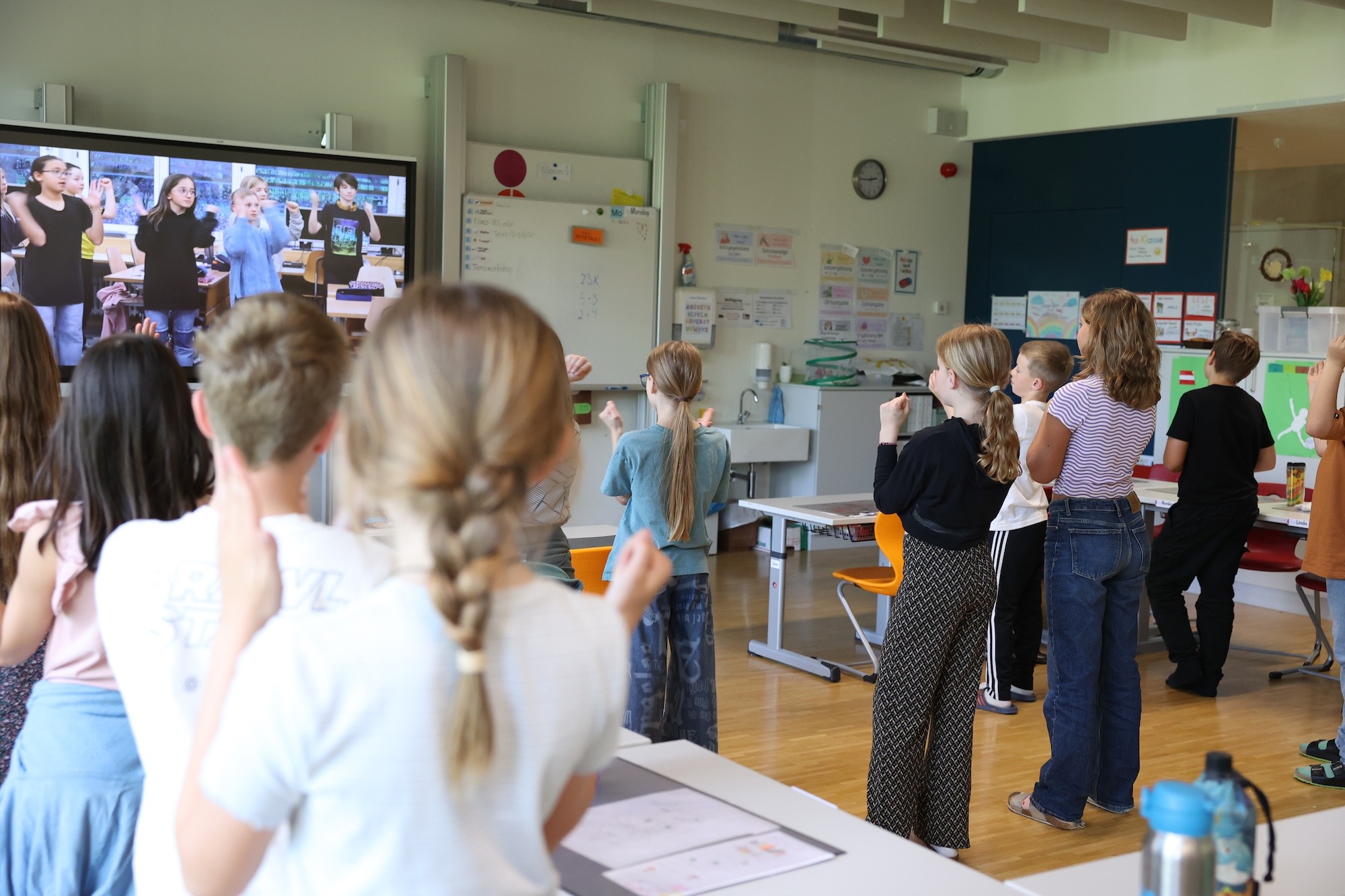 Schüler*innen folgen in einem Klassenzimmer einem digitalen Tanzvideo auf einem großen Bildschirm – moderne Tanzvermittlung mit groove2grow.