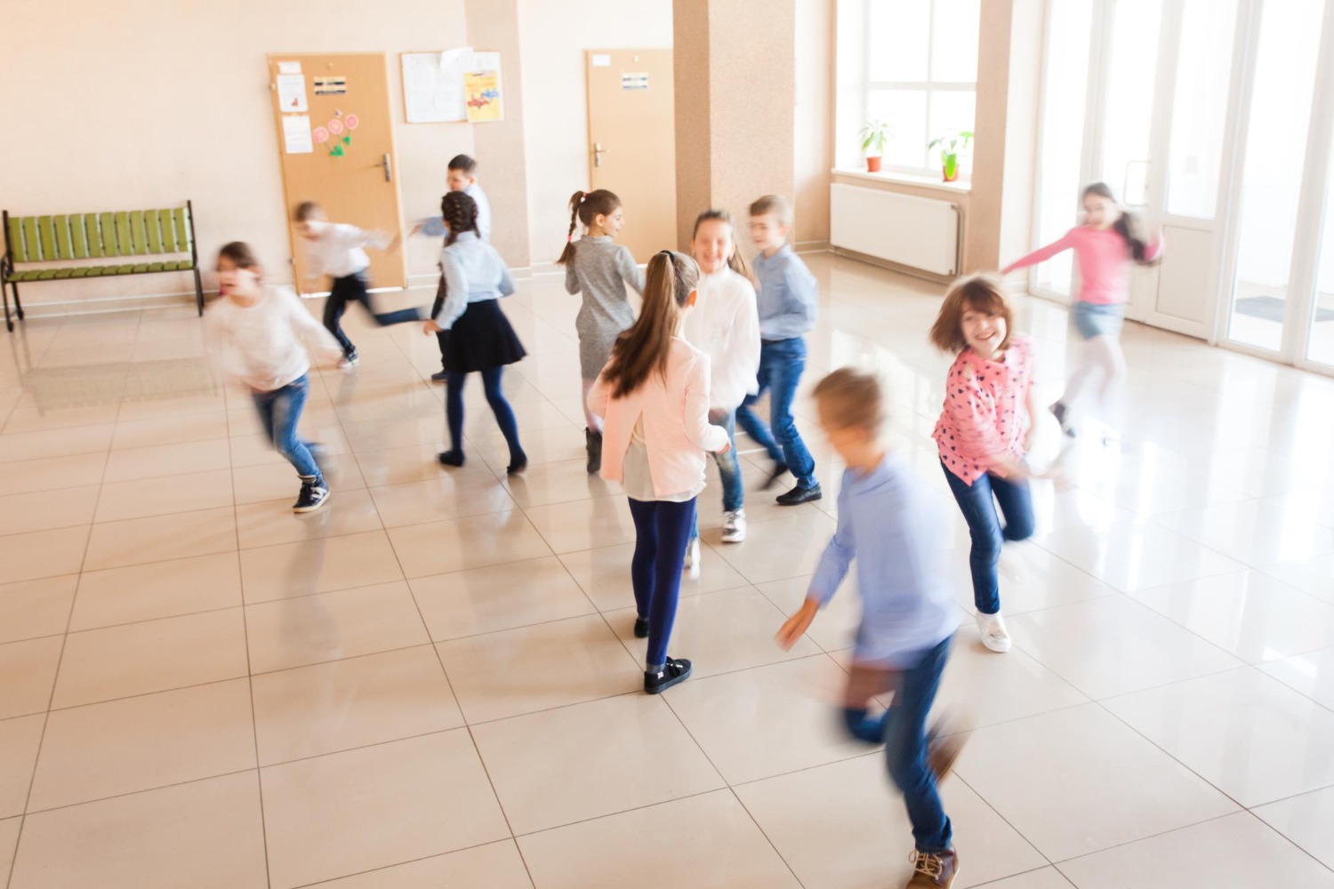 Verschwommene Aufnahme von spielenden und rennenden Kindern in einem hellen Schulflur – Ausdruck von Energie und Bewegungsdrang.