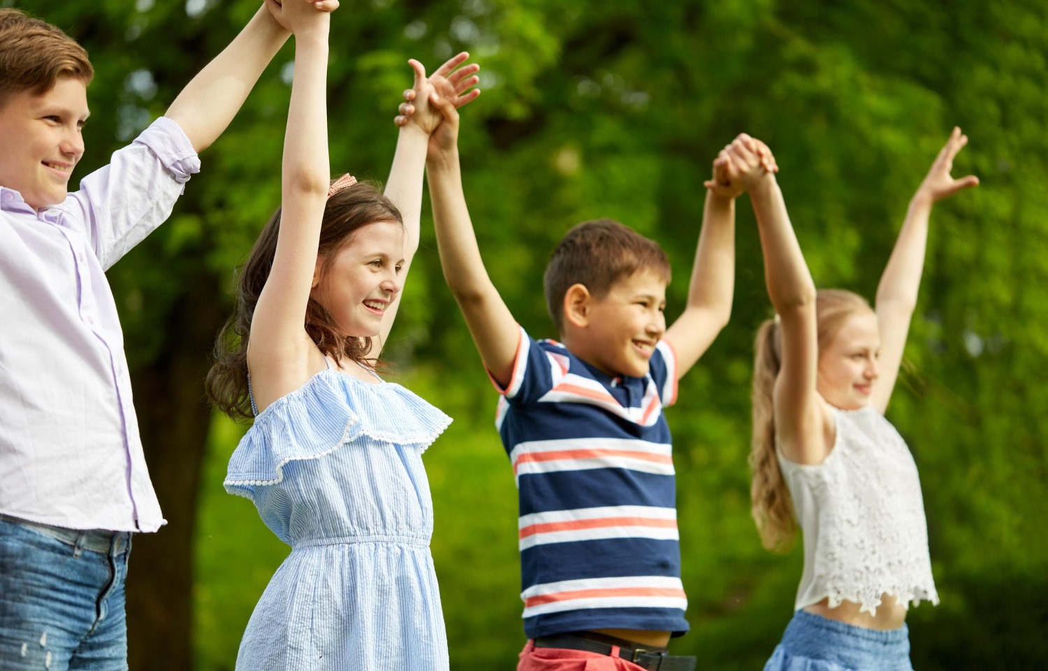 Vier glückliche Schulkinder halten im Freien die Hände hoch und zeigen soziale Synchronisation und Shared Intentionality im groove2grow Unterricht.